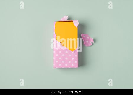 Partially unwrapped bright yellow rectangular box in pink polka dot wrapping paper on a pastel green background, symbolizing a cheerful gift or produc Stock Photo