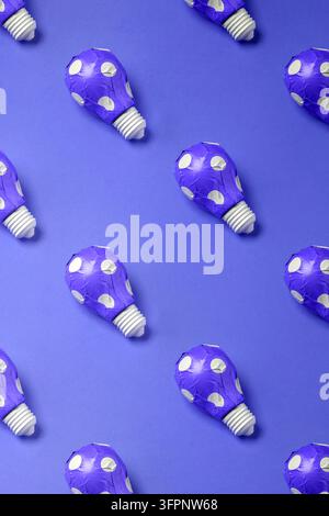Creative pattern with light bulbs wrapped in purple polka dot gift paper on a blue background. Modern and stylish abstract background. Stock Photo