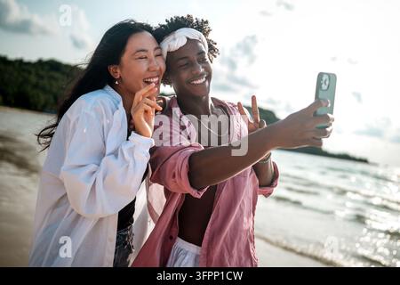 Trendy digital creator couple taking selfie by the beach, sharing travel content for social media Stock Photo