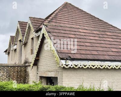 old abandoned brick house with brown tiled roof, weathered decorative white wooden fascia boards, exterior architectural view, vintage real estate Stock Photo
