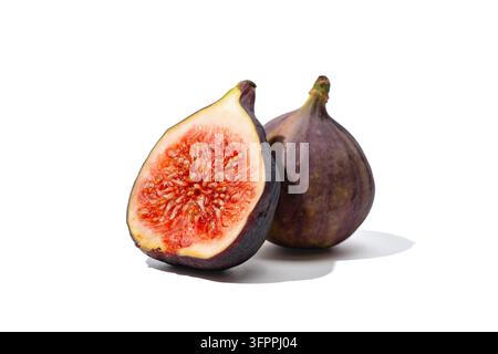 A halved fig with red seeded pulp stands in front of a whole purple fig with stem, isolated on white with soft shadows. Stock Photo
