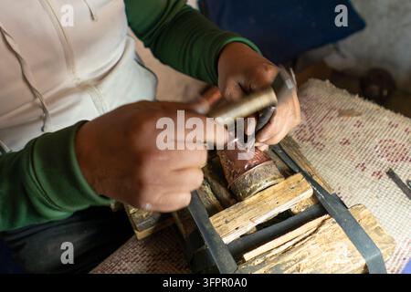 Close up of a skilled artisan hand hammering intricate floral patterns into a copper metal vessel Stock Photo