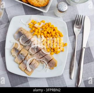Slices of spicy marinated herring fillet with corn and onion Stock Photo
