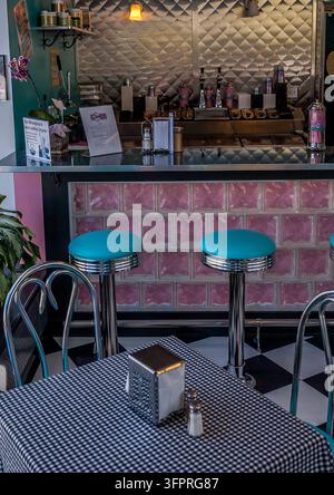View of the interior of an iconic diner featuring a counter with pink glass blocks, turquoise stools, and a table with a checkered tablecloth in Arlin Stock Photo