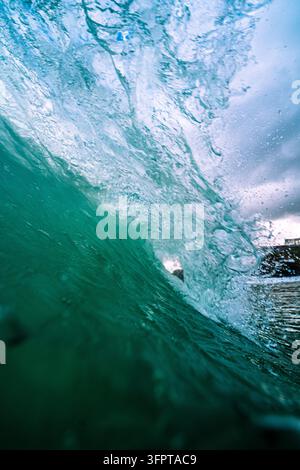View of a powerful turquoise ocean wave breaking with white sea foam and spray in United Kingdom. Stock Photo