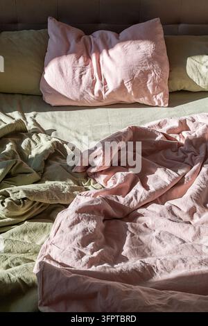 Rest and Relaxation. Unmade Bed with Soft Linen Bedding in Morning Sunlight for Home Comfort and Wellness Lifestyle Stock Photo
