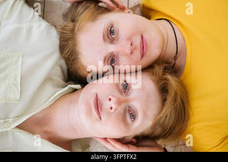 Two red-haired sisters lie cheek to cheek and look at the camera. Similar women with fair skin and freckles. Beautiful twin women. Stock Photo