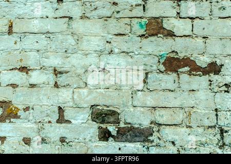Rustic and aged brick wall surface covered in cracked, peeling light green and teal paint, revealing weathered brown bricks underneath. Abstract backg Stock Photo