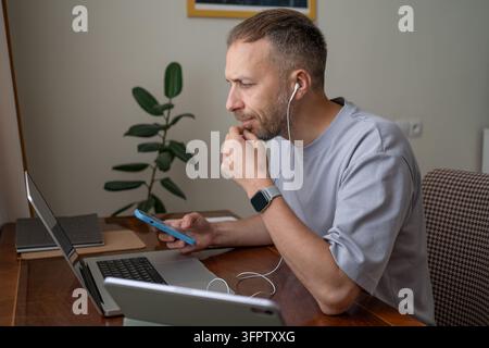 Multitasking worker managing laptop smartphone tablet and technology devices, productivity workflow focus across several screens during remote professional work at home. Stock Photo