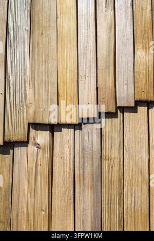 Closeup of natural wooden wall cladding made of overlapping vertical timber planks in sunlight, rustic wood grain texture with warm beige tones and Stock Photo