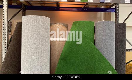 Rolls of outdoor carpet and artificial grass in different colors displayed on metal shelves in home improvement store Stock Photo