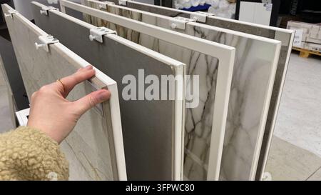 Customer examining large marble effect porcelain tiles on display rack in home improvement store . High quality photo Stock Photo