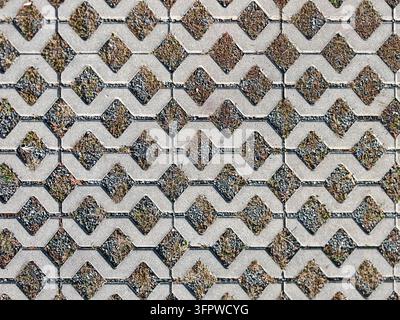 Geometric pattern of grey concrete permeable paving blocks with growing grass and gravel in the gaps, serving as an eco-friendly driveway texture. Stock Photo