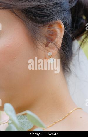 Ear wearing earrings, in outdoor, with ear, earrings, necklace, hair, from a close-up perspective, with gold, white accents, and elegant mood, showing Stock Photo