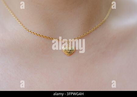 Woman wearing a heart-shaped pendant necklace, in close-up of the neck area, with heart-shaped pendant, gold chain, from a close-up top-down view Stock Photo