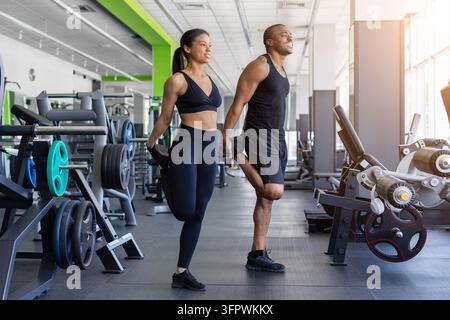 Athletic black couple performing standing quadriceps stretches together in modern gym Stock Photo