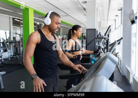 Black man adjusting treadmill settings while woman runs beside him in gym Stock Photo