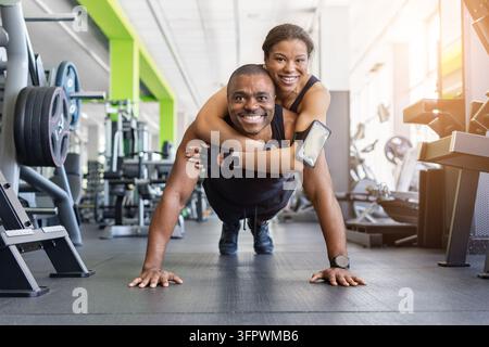 Happy black couple doing push-ups in gym, woman hugging man from behind Stock Photo