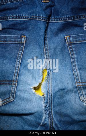 Closeup of a pair of old, worn-out blue jeans on a yellow table. Torn trousers. Hole in the seat. Stock Photo