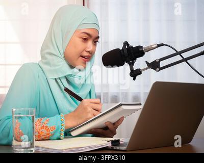 Good looking young muslim female making an online podcast recording for her online show. Attractive Asian muslim business woman using computer laptop Stock Photo