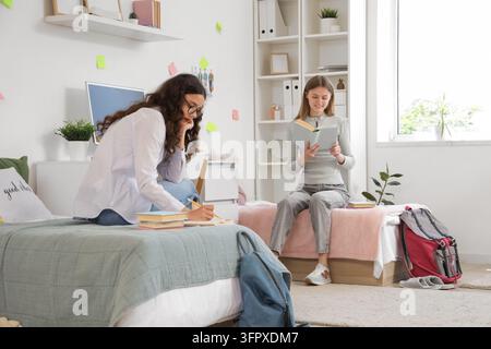 Education and academic success, two female students studying together in a shared dormitory room with books and laptop for college exam preparation Stock Photo