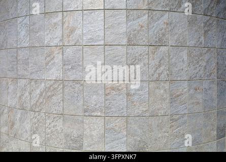 Curved wall clad in vertical stone-look porcelain tiles. The rectangular tiles feature a textured of gray-beige natural stone  arranged in grid patter Stock Photo