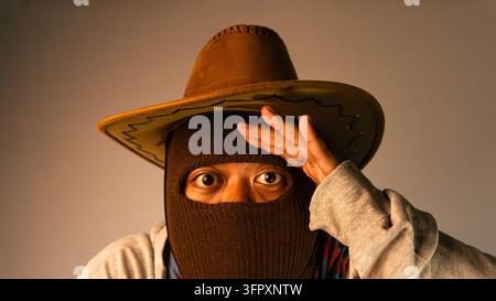 Creative visual displaying one young Asian male holding a flat hand above his eyes in a searching or saluting gesture. The anonymous subject wears a c Stock Photo