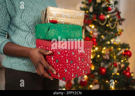 Person holding stacked Christmas gifts near festive tree Stock Photo