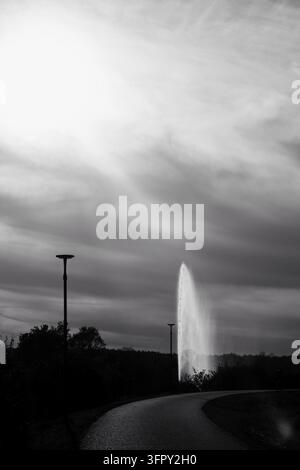 Majestic water fountain silhouette spraying high against a dramatic sunny sky in black and white Stock Photo