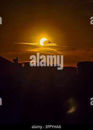 A striking scene of a partially obscured sun, possibly during an eclipse or atmospheric phenomenon, casting an intense orange and yellow glow across t Stock Photo