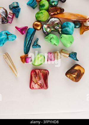 An overhead close-up shot of various brightly colored, smooth, and irregular-shaped beads, primarily made from mother-of-pearl or shell materials, sca Stock Photo