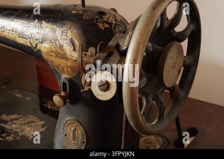 A detailed close-up shot of an antique sewing machine, showcasing its intricate gold and black ornate patterns. The focus is on the textured hand whee Stock Photo