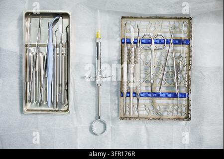 Dental instruments arranged on sterile surface in clinic. Top view of mirror, probes, scalers, syringe and surgical tools for examination, treatment, periodontology concept Stock Photo