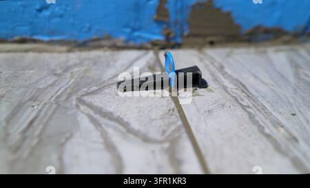 Close up on tile leveling clip and wedge system used for laying floor tiles. Wet mortar is visible in grout lines and on blue waterproofing membrane o Stock Photo