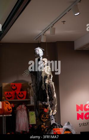 Halloween decorations including hanging skeletons, a grim reaper, pumpkin buckets and spooky costumes displayed inside a retail shop. Stock Photo