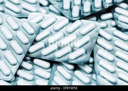 Silver blister packs filled with white pharmaceutical capsules in closeup. Medicine background for medication supply, healthcare and drug treatment. Stock Photo