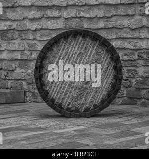 A striking black and white close-up image of a circular stone millstone, featuring distinct diagonal grooves, leaning against a textured brick wall. T Stock Photo