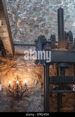 A close-up shot capturing a complex assembly of dark metal industrial gears and a large threaded screw mechanism, juxtaposed with a rustic wooden beam Stock Photo