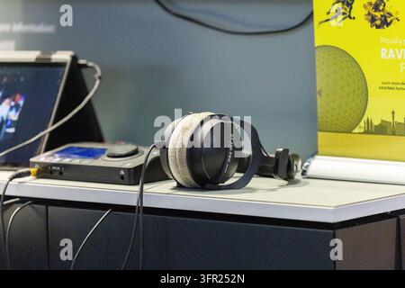 Amsterdam, Netherlands - September 11, 2026: Over ear headphones lie beside electronic equipment and a tablet on a counter beneath promotional exhibit Stock Photo