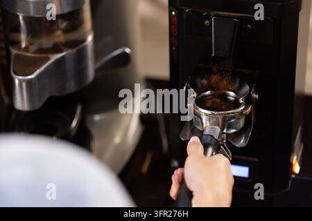 Asian woman holding portafilter catching coffee grounds from grinder at coffee bar, copy space Stock Photo