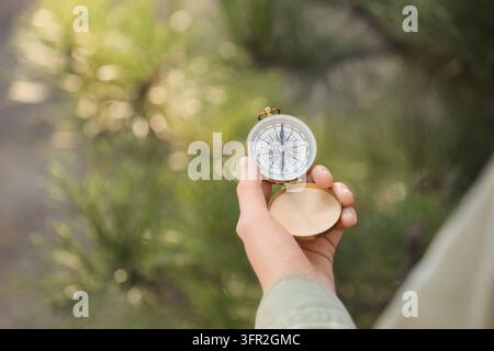 Direction and guidance concept, person holding a vintage brass compass for navigation and travel planning in a forest with soft natural sunlight Stock Photo