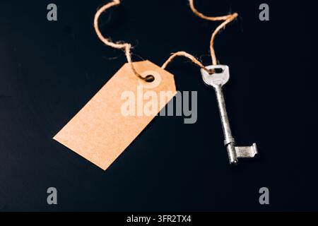 Silver key on twine with a blank kraft paper tag on a dark background, copy space. Concept of mortgage, savings and new home. Stock Photo