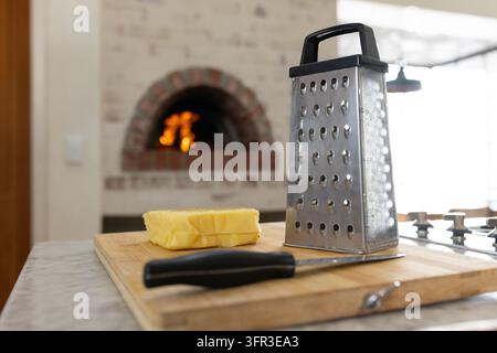 Stainless steel four sided box grater standing on wood board by oven flame, with butter Stock Photo