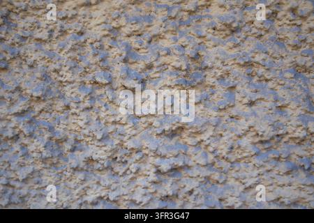 Rough beige and blue-gray plaster wall with an uneven granular surface and abstract texture. Stock Photo