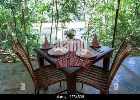 Served table and two rattan chairs in an empty restaurant terrace. Tanzania, east Africa Stock Photo