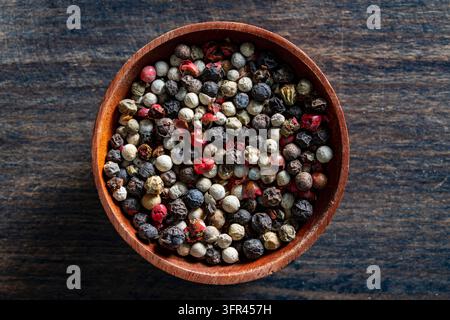 Peppercorn mix in wooden bowl close up top view. Top view of colorful pepper blend in small wood bowl. Mix of black white green and pink peppercorns o Stock Photo