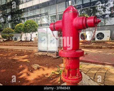 A bright red fire hydrant stands on a paved sidewalk outside a modern glass office building, illustrating urban fire protection and public safety infr Stock Photo