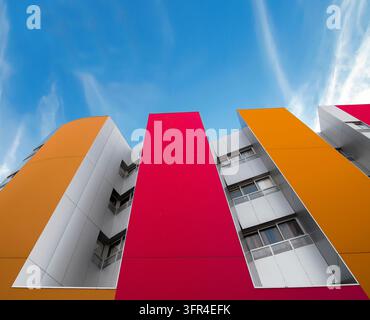 View of a colorful building with windows and metallic shapes, set against a blue sky with clouds. Stock Photo