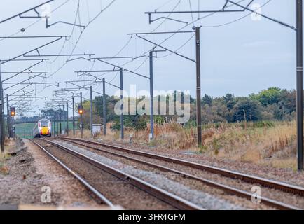 Azuma electrified train passing through the Victorian stone built Acklington  railway station on the east coast mainline. Stock Photo
