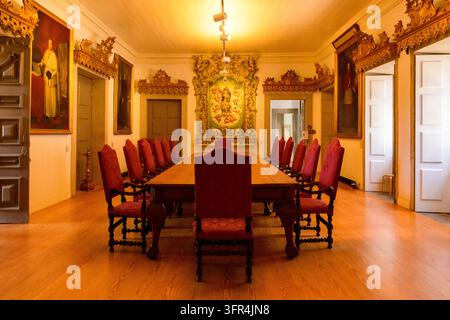 Porto, Portugal - May 27, 2019: A long wooden table with red upholstered chairs stands in an ornate meeting room with framed paintings and carved deco Stock Photo